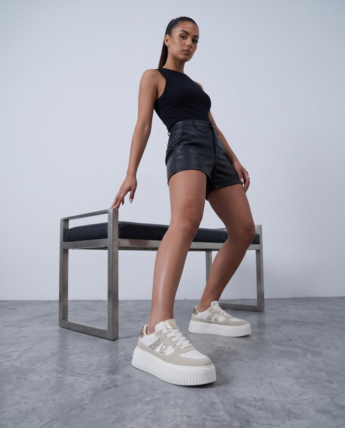 Modella in piedi con shorts neri e sneakers platform bianche/beige con glitter e dettaglio leopardato.