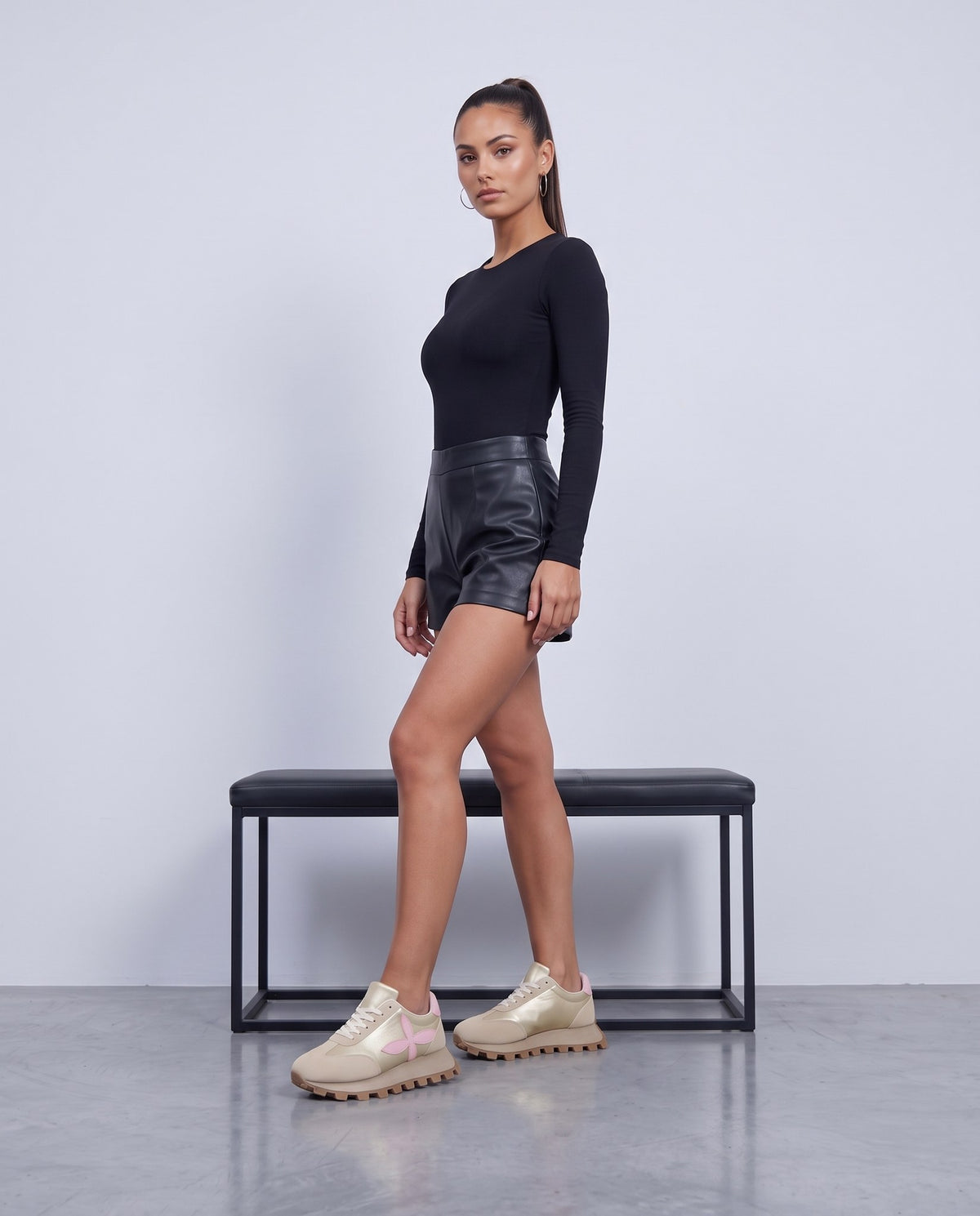 Modella in piedi, sneaker beige con fiore rosa, posa a passo in studio grigio chiaro
