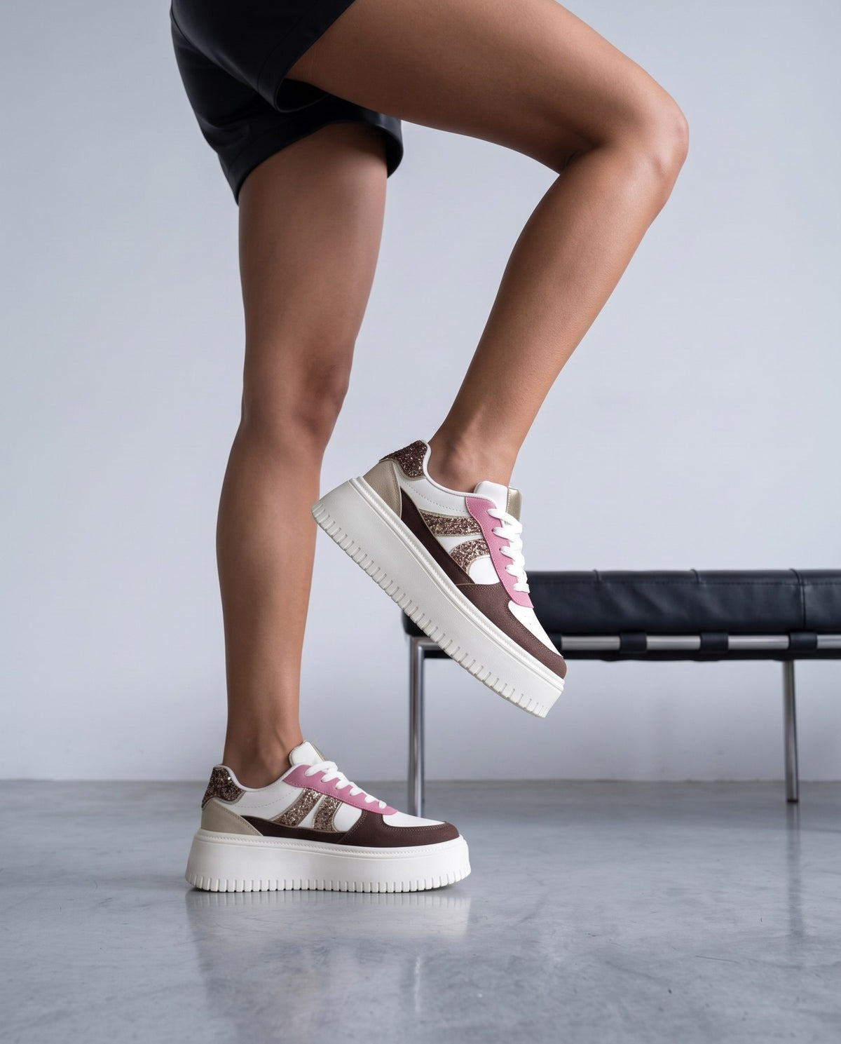 Dettaglio sneaker platform marrone, bianco e glitter rosa su gambe in primo piano
