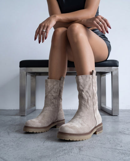 Modella seduta su panca, stivali in camoscio khaki/beige con suola carrarmato in primo piano.