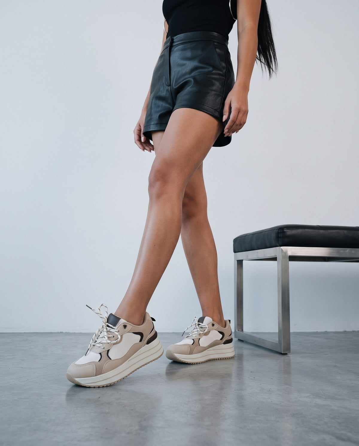 Donna in shorts neri che cammina con sneaker platform beige e bianche, vicino a una panca.