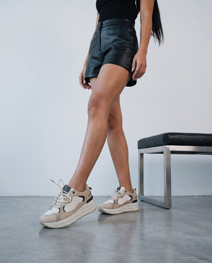 Donna in shorts neri che cammina con sneaker platform beige e bianche, vicino a una panca.