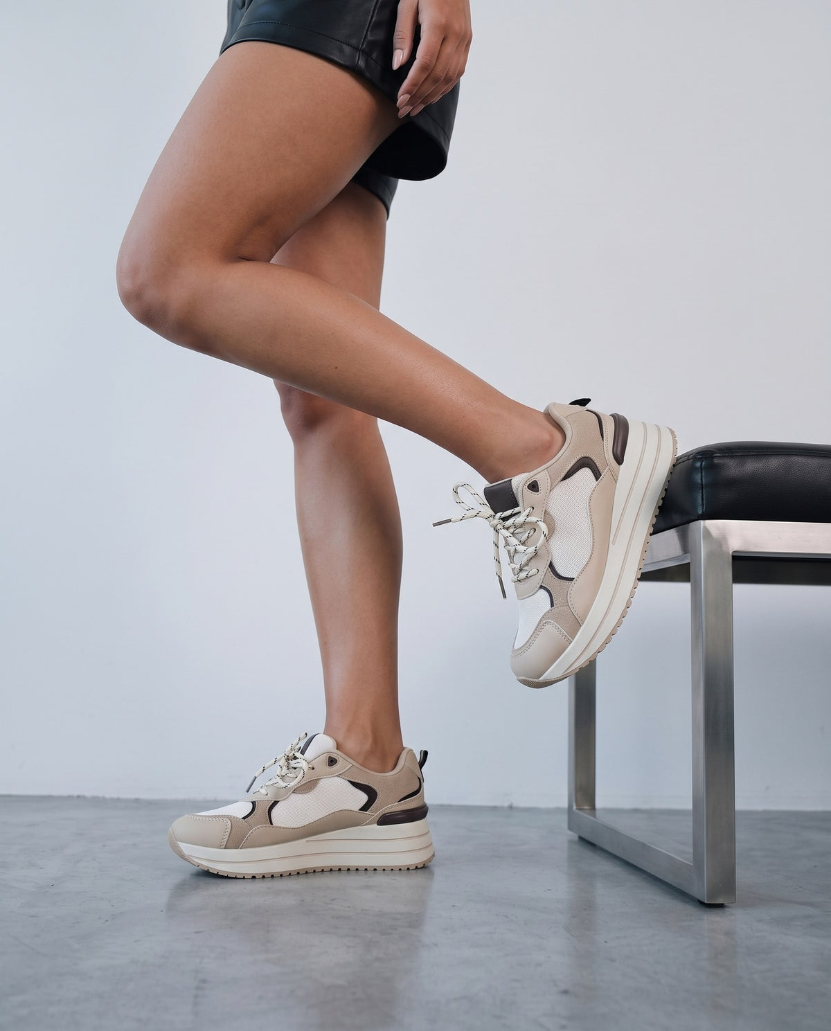 Gambe femminili con sneaker platform beige e bianca, dettaglio laterale ravvicinato su sfondo neutro.