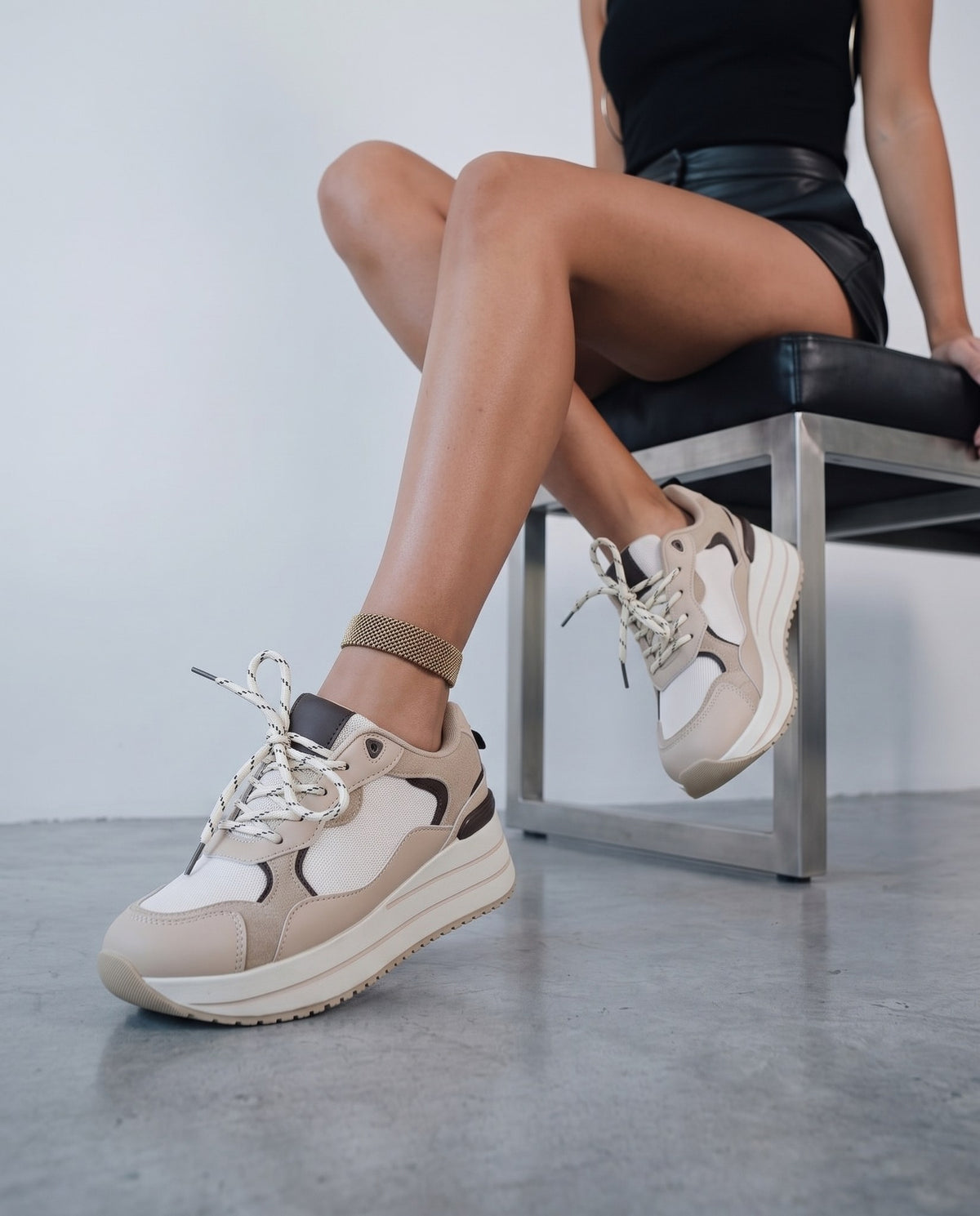 Donna seduta su sgabello, gambe accavallate, sneakers beige platform con dettagli bianchi e marroni.