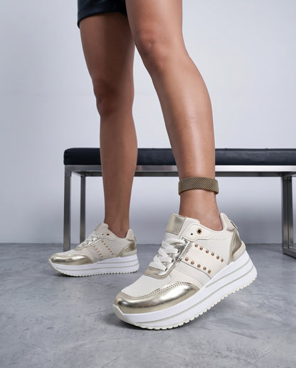 Primo piano di gambe con sneaker beige e oro, panca metallica sullo sfondo sfocato.