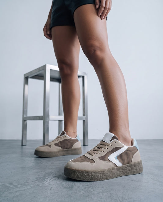 Dettaglio ravvicinato di sneaker khaki bicolore con suola platform, gambe in piedi su pavimento in studio