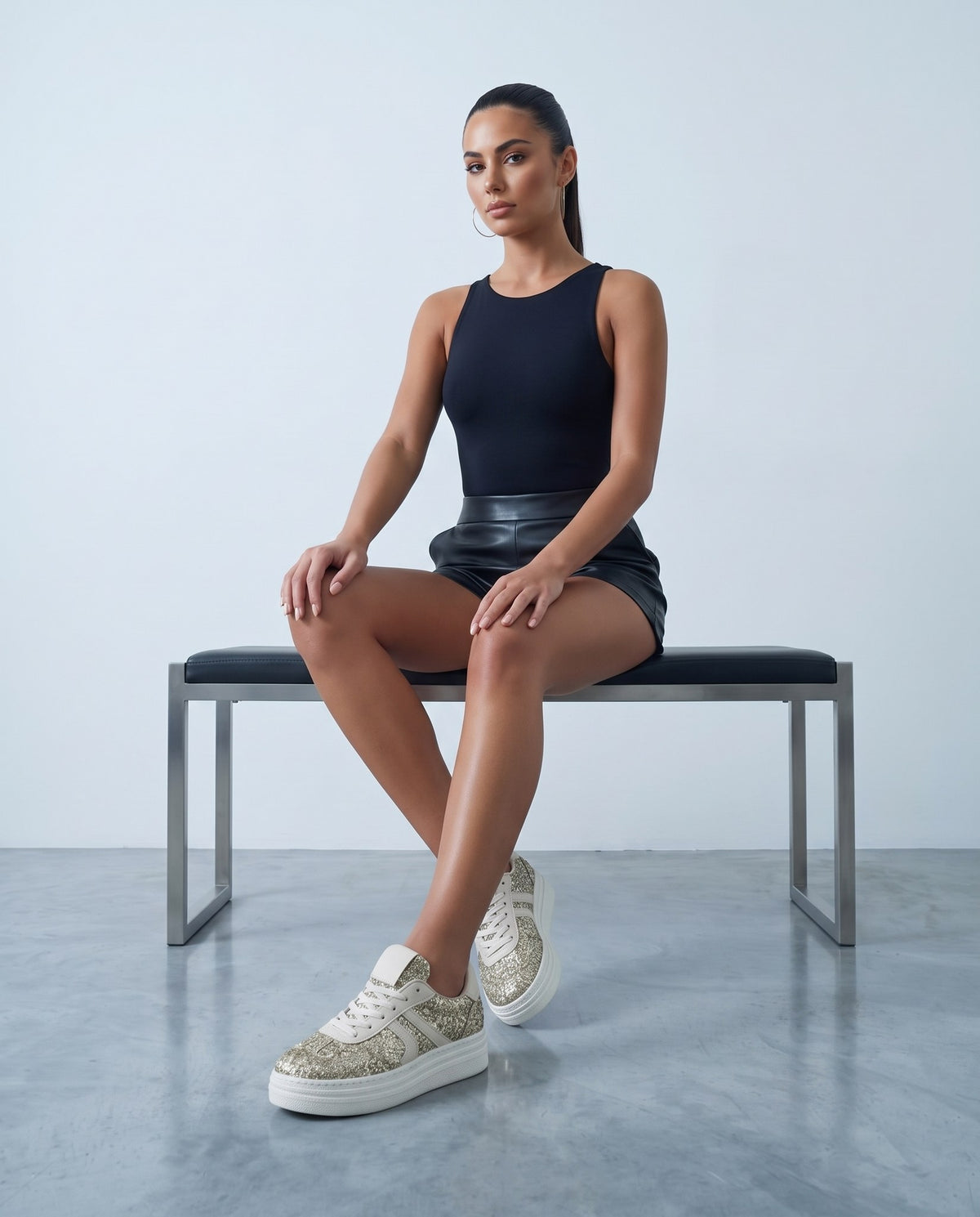Modella seduta su panca con sneakers glitter oro e suola platform bianca, primo piano dal basso