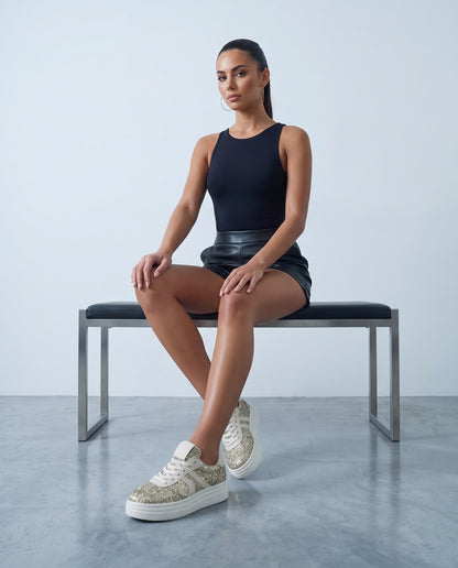 Modella seduta su panca con sneakers glitter oro e suola platform bianca, primo piano dal basso