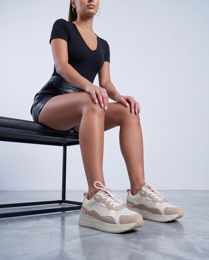 Modella seduta su panca nera, sneakers rosa-beige platform in primo piano, gambe distese verso la camera.