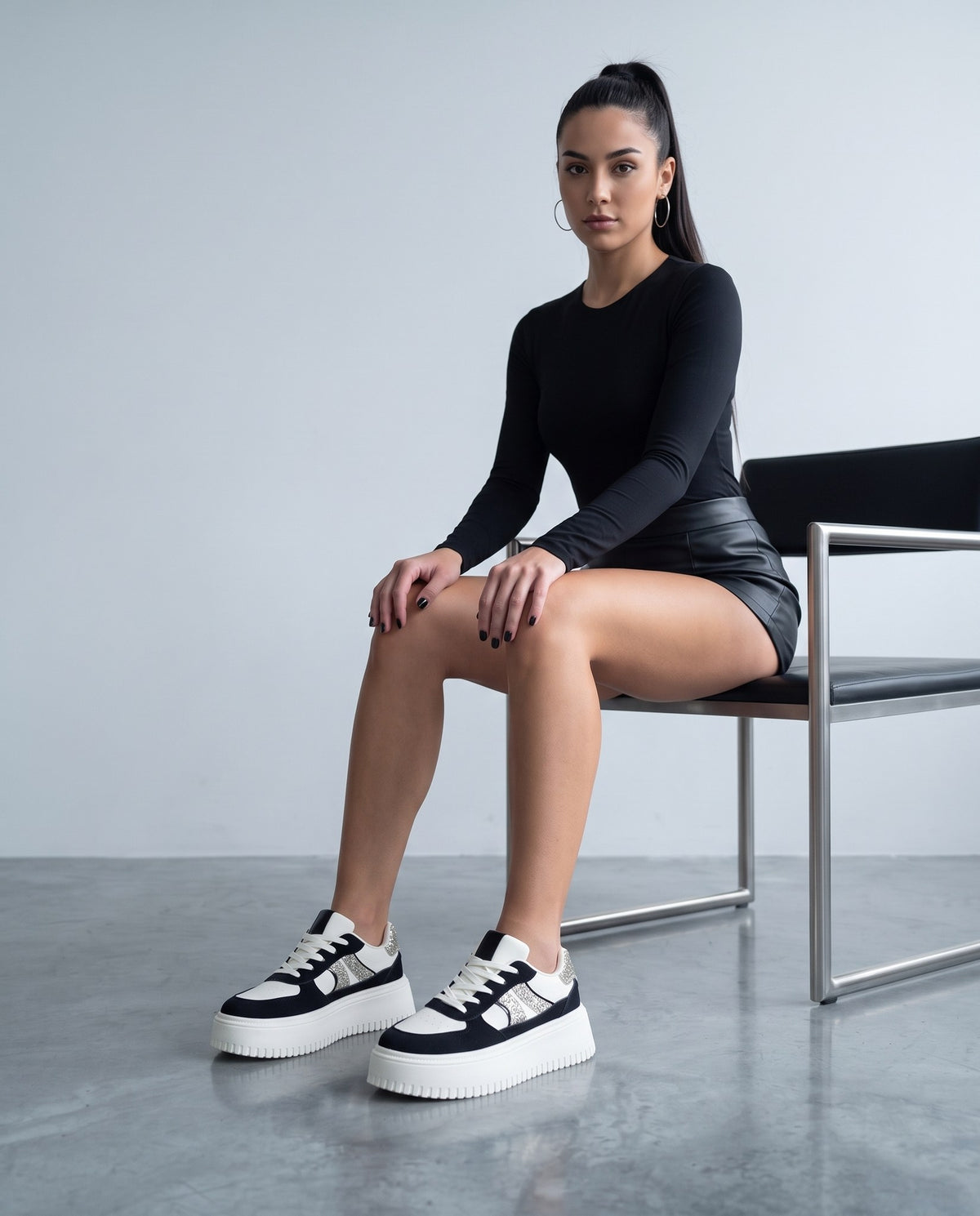 Modella seduta con sneakers bianche e nere glitter in primo piano, gambe distese verso la camera