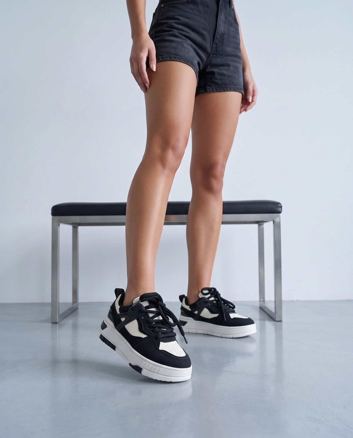 Gambe femminili con sneakers bicolore nero e bianco accanto a panca in acciaio e pelle nera