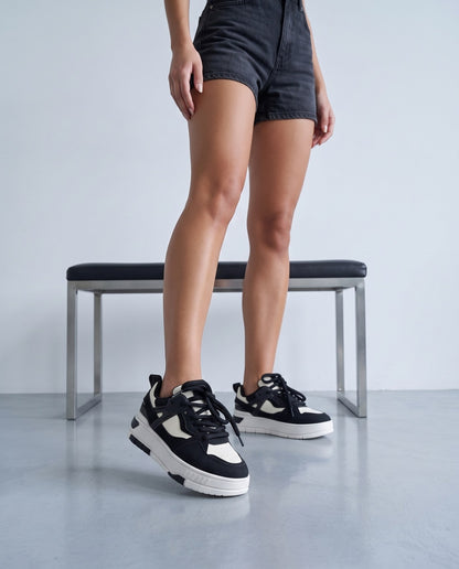Gambe femminili con sneakers bicolore nero e bianco accanto a panca in acciaio e pelle nera