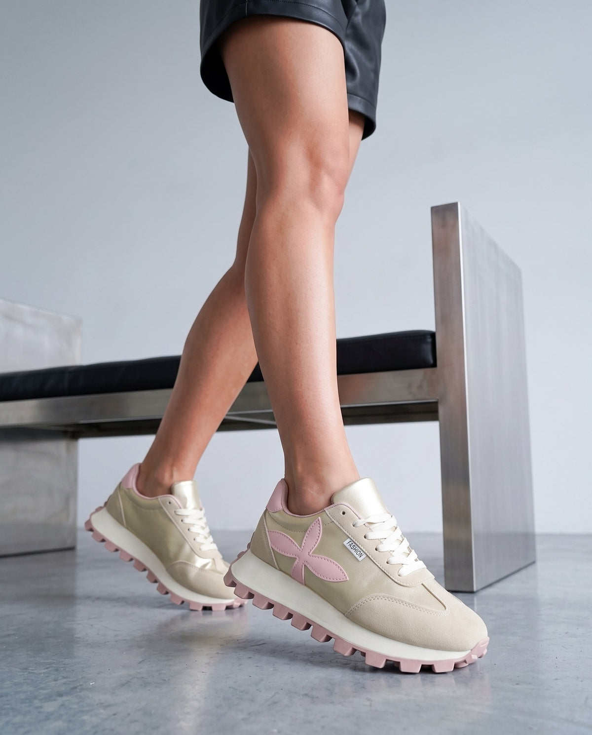 Primo piano delle gambe e delle sneaker oro/rosa in movimento, vicino a una panca in metallo e pelle