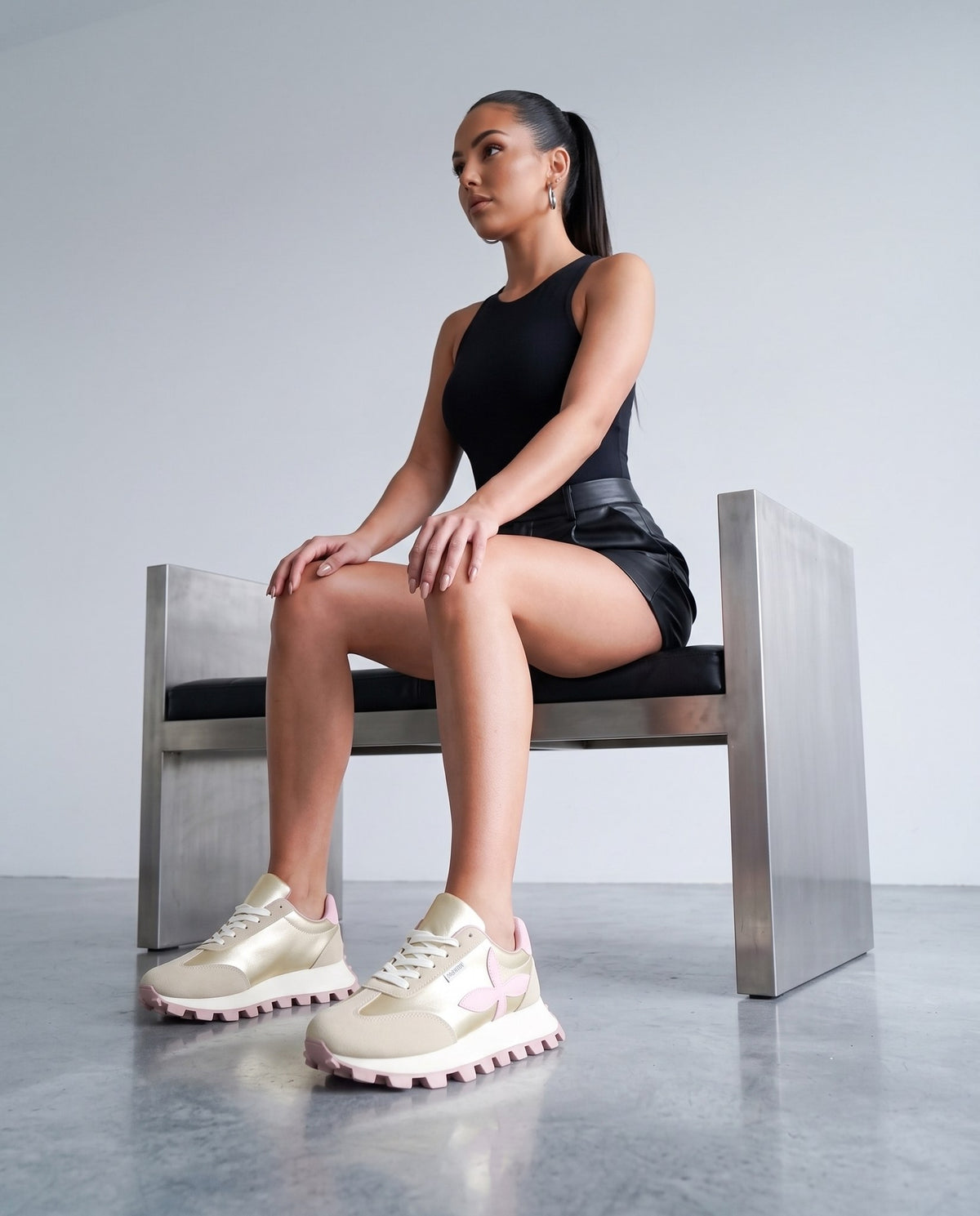 Modella seduta su panca, scarpe sneaker dorate con fiore rosa in primo piano