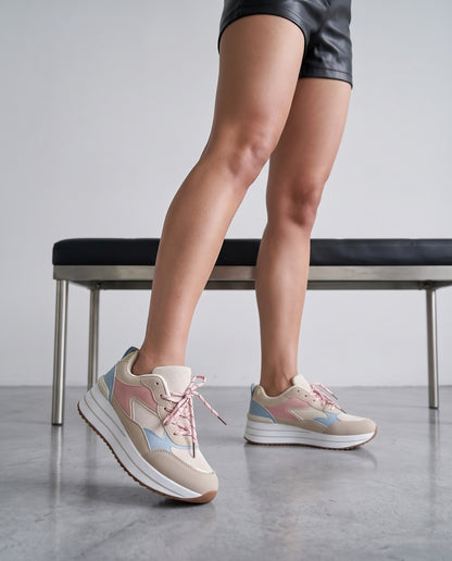 Primo piano di gambe con sneakers beige dai dettagli rosa e azzurro, panca in sottofondo.