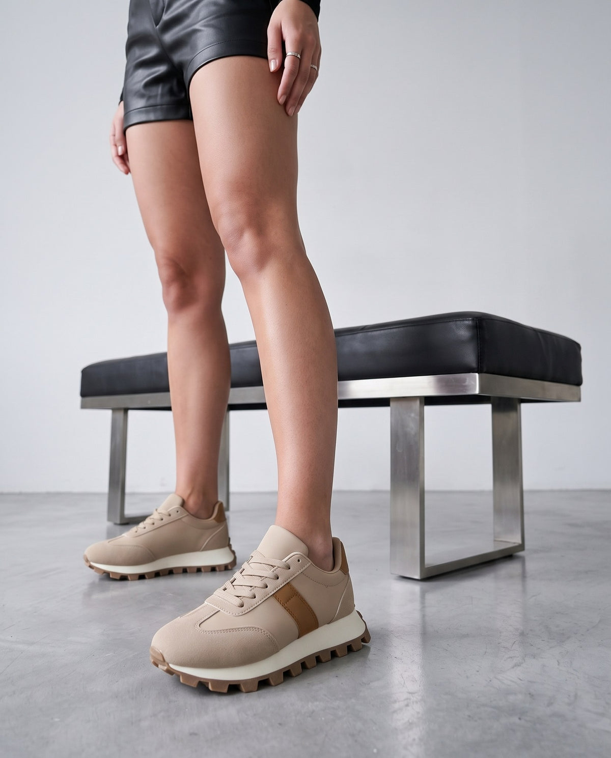 Dettaglio ravvicinato di sneakers beige con banda cammello, panca nera sullo sfondo