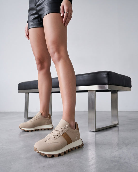 Dettaglio ravvicinato di sneakers beige con banda cammello, panca nera sullo sfondo