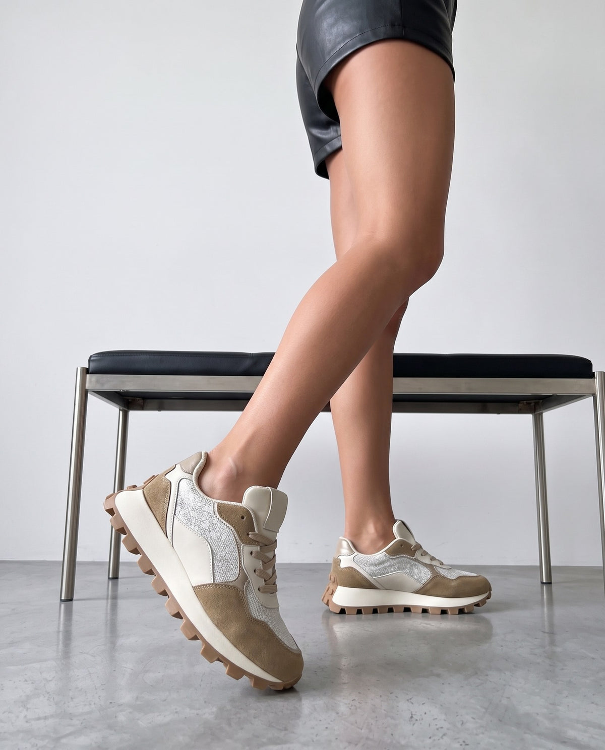 Dettaglio ravvicinato delle gambe e delle sneaker bicolore khaki e bianco durante il passo, panca sullo sfondo.