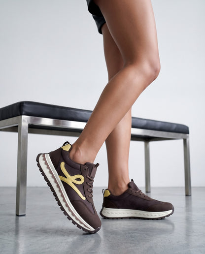 Dettaglio ravvicinato di gambe e sneaker marroni con fiocco giallo, panca sullo sfondo sfocata