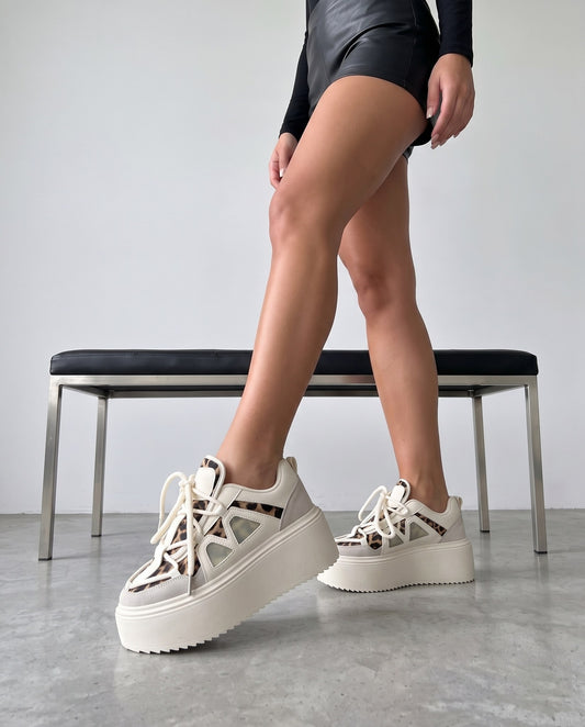 Gambe della modella con sneaker platform bianche e maculate, panca in acciaio e pelle nera sullo sfondo