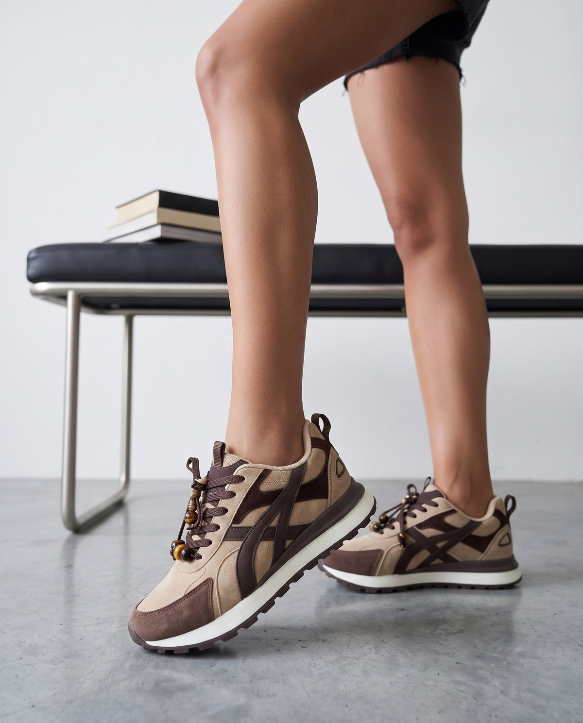 Dettaglio ravvicinato delle gambe e di un paio di sneakers beige e marrone con charm di perline sui lacci