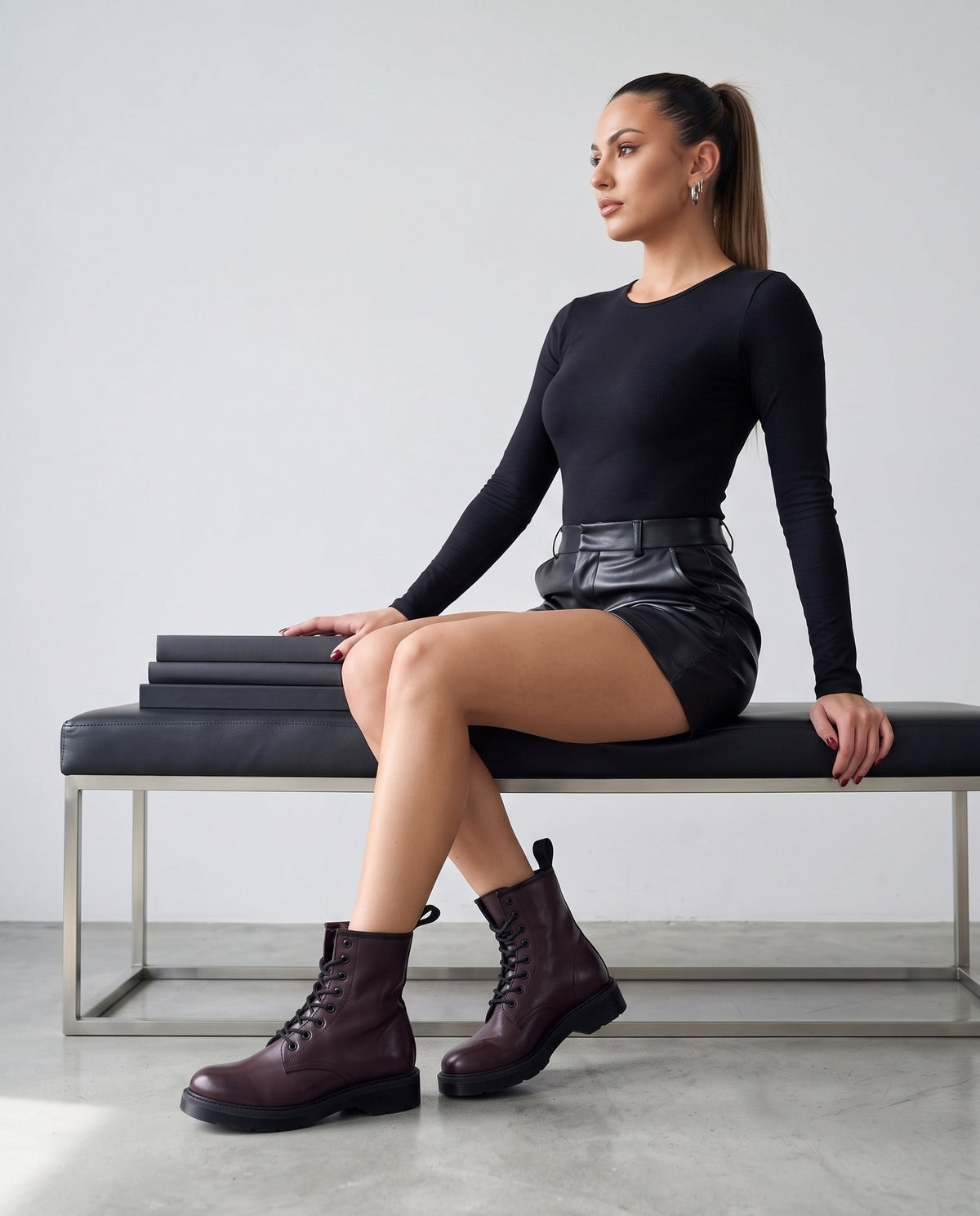 Modella seduta su panca con stivaletti bordeaux in pelle, gambe incrociate, stile sportivo chic