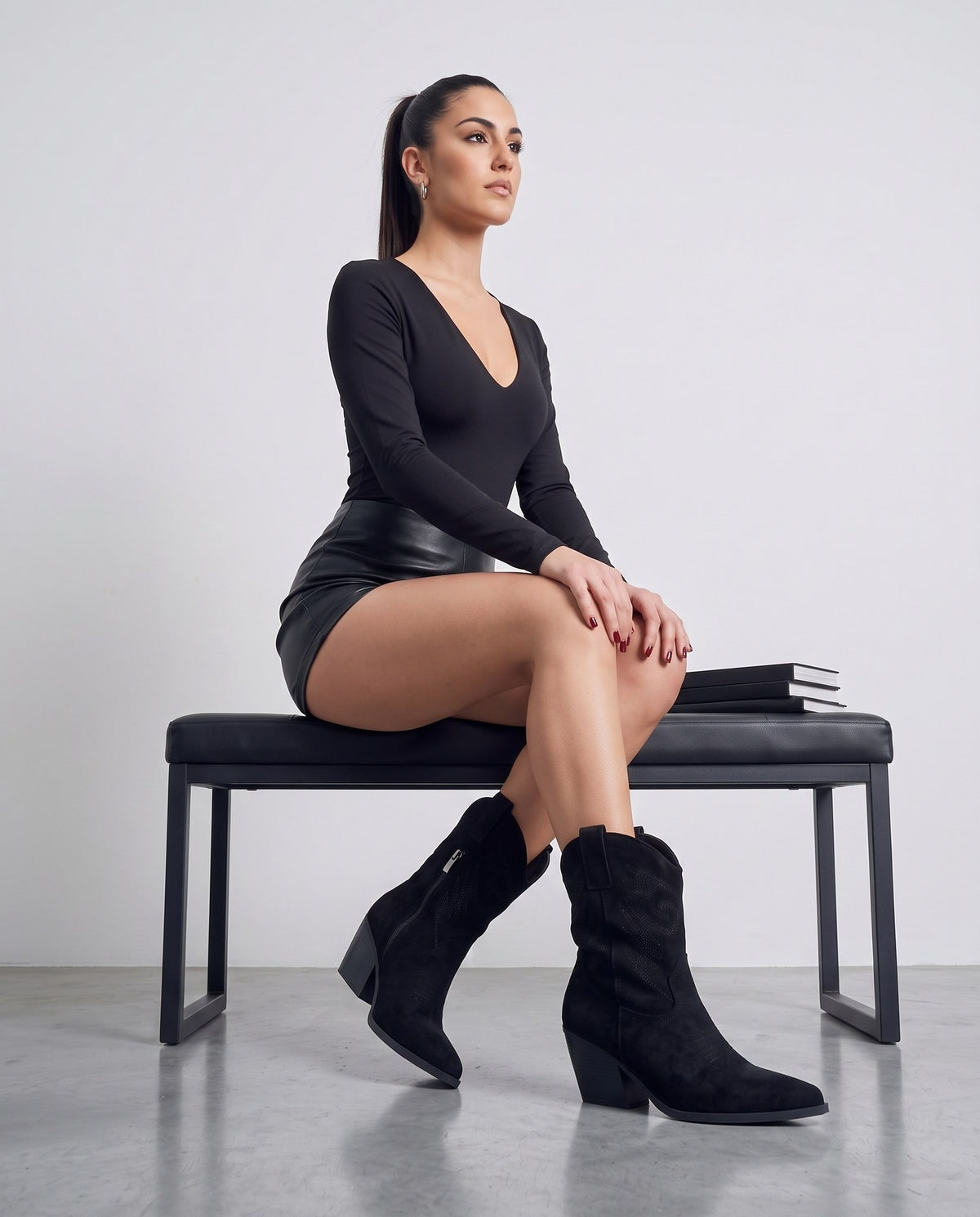 Modella seduta su panca nera, gambe accavallate, indossa stivaletti camperos neri in camoscio.