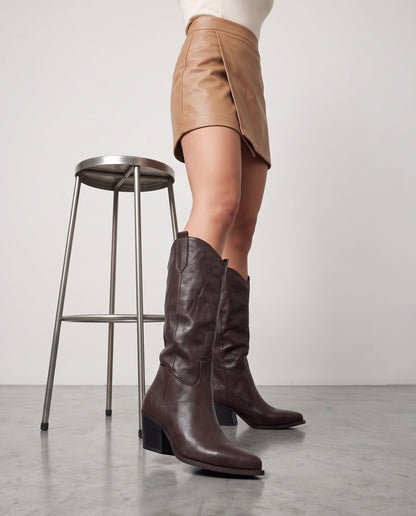 Gambe con stivali cowboy testa di moro, accanto a sgabello in metallo, pavimento in cemento grigio