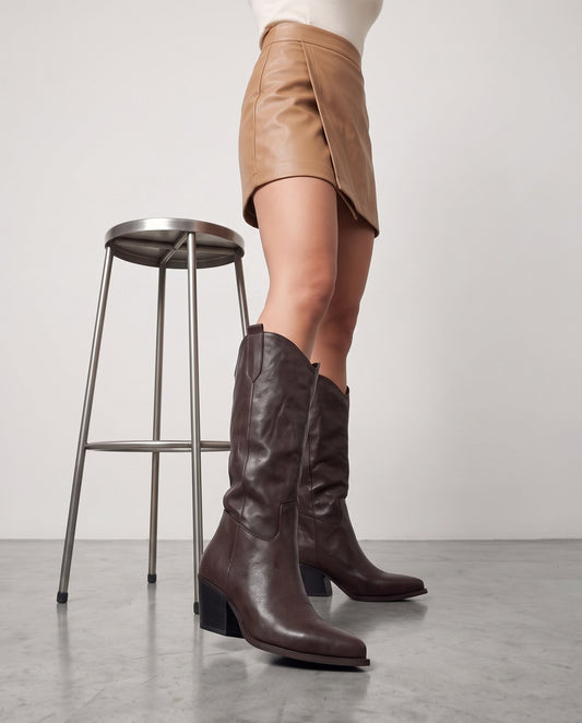 Gambe con stivali cowboy testa di moro, accanto a sgabello in metallo, pavimento in cemento grigio