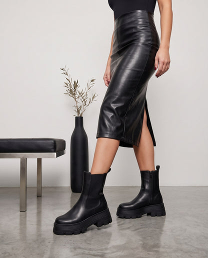 Stivaletti chelsea neri con suola carrarmato, modella in gonna in ecopelle, gambe in piedi