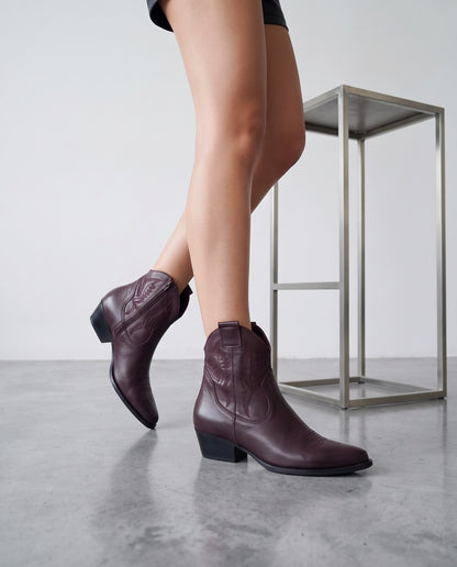 Gambe in posa di cammino con stivaletti texani bordeaux, tavolino in acciaio sullo sfondo