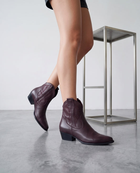 Gambe in posa di cammino con stivaletti texani bordeaux, tavolino in acciaio sullo sfondo
