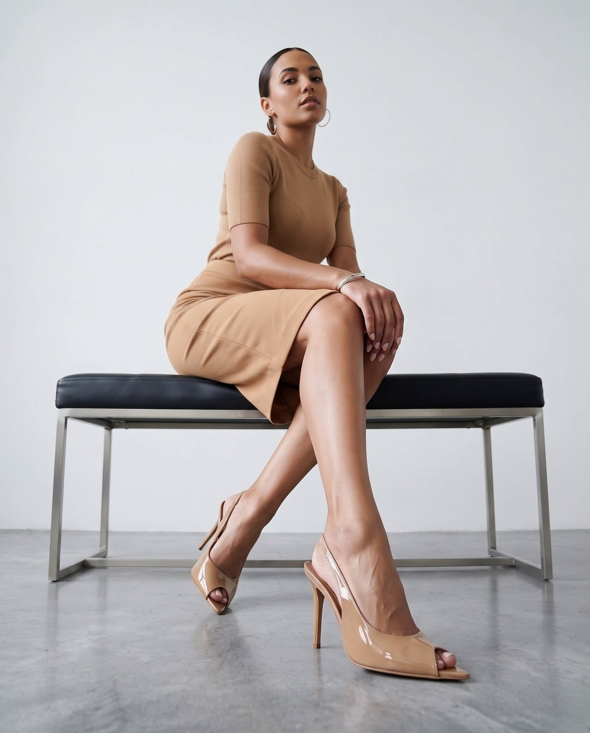 Modella seduta su panca, gambe accavallate, sandali slingback beige in vernice in primo piano