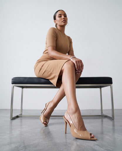 Modella seduta su panca, gambe accavallate, sandali slingback beige in vernice in primo piano