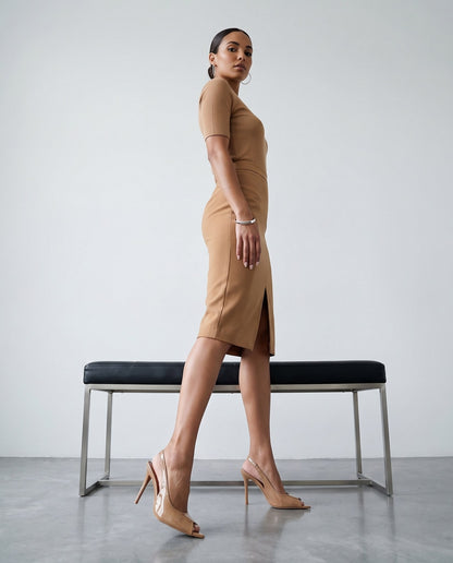 Modella di profilo con tubino cammello e décolleté slingback beige vicino a panca nera e cromata