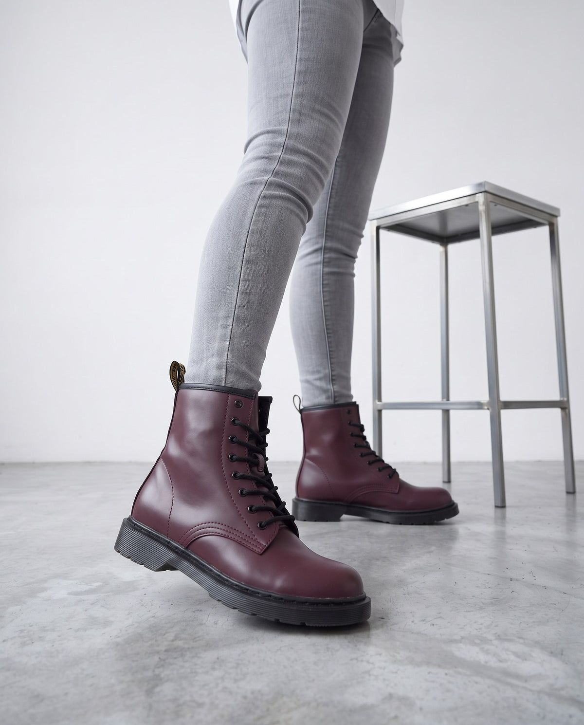 Primo piano di gambe con jeans grigi e stivaletti bordeaux in ecopelle accanto a uno sgabello cromato