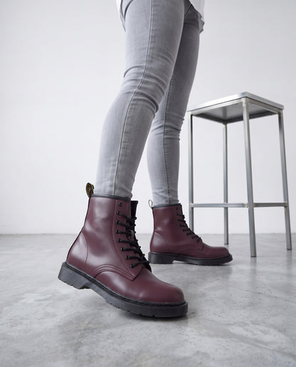 Primo piano di gambe con jeans grigi e stivaletti bordeaux in ecopelle accanto a uno sgabello cromato