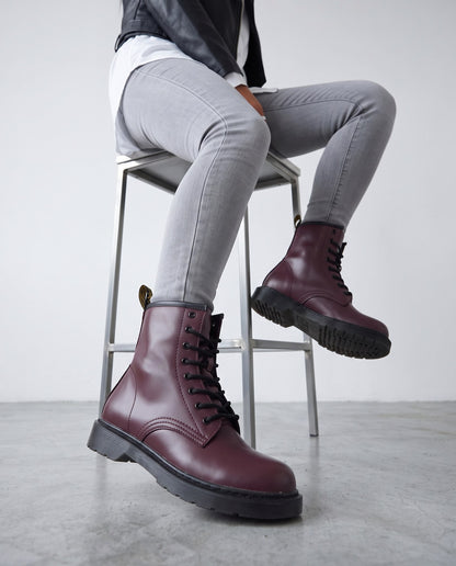 Modella seduta su sgabello cromato con stivaletti bordeaux stile combat boot, gamba piegata e gamba distesa