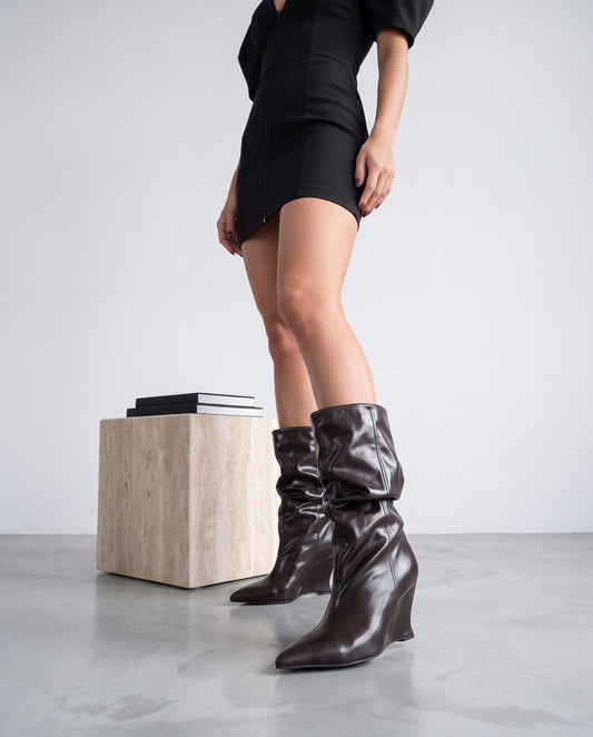 Gambe in piedi con stivali marroni a zeppa, cubo di travertino con libri sullo sfondo