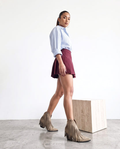 Modella di profilo con stivaletti khaki a frange, camicia a righe e minigonna bordeaux, in cammino