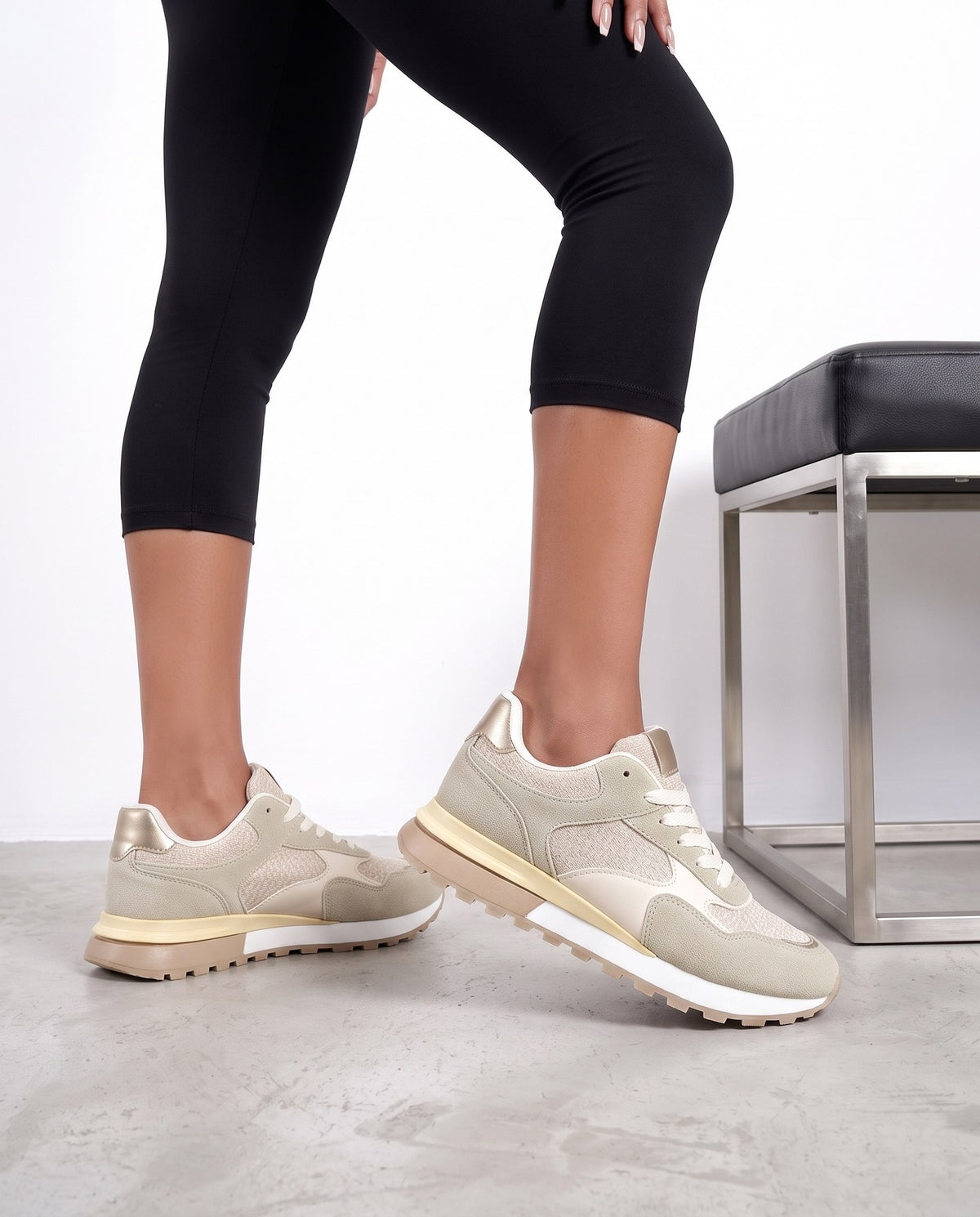 Gambe di modella in piedi con sneakers beige e panchina nera sullo sfondo