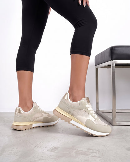 Gambe di modella in piedi con sneakers beige e panchina nera sullo sfondo