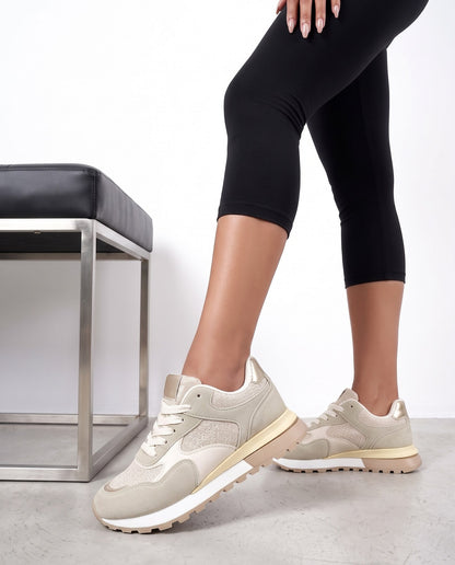 Primo piano di gambe con sneakers beige, una scarpa vicino alla camera appoggiata su panca nera