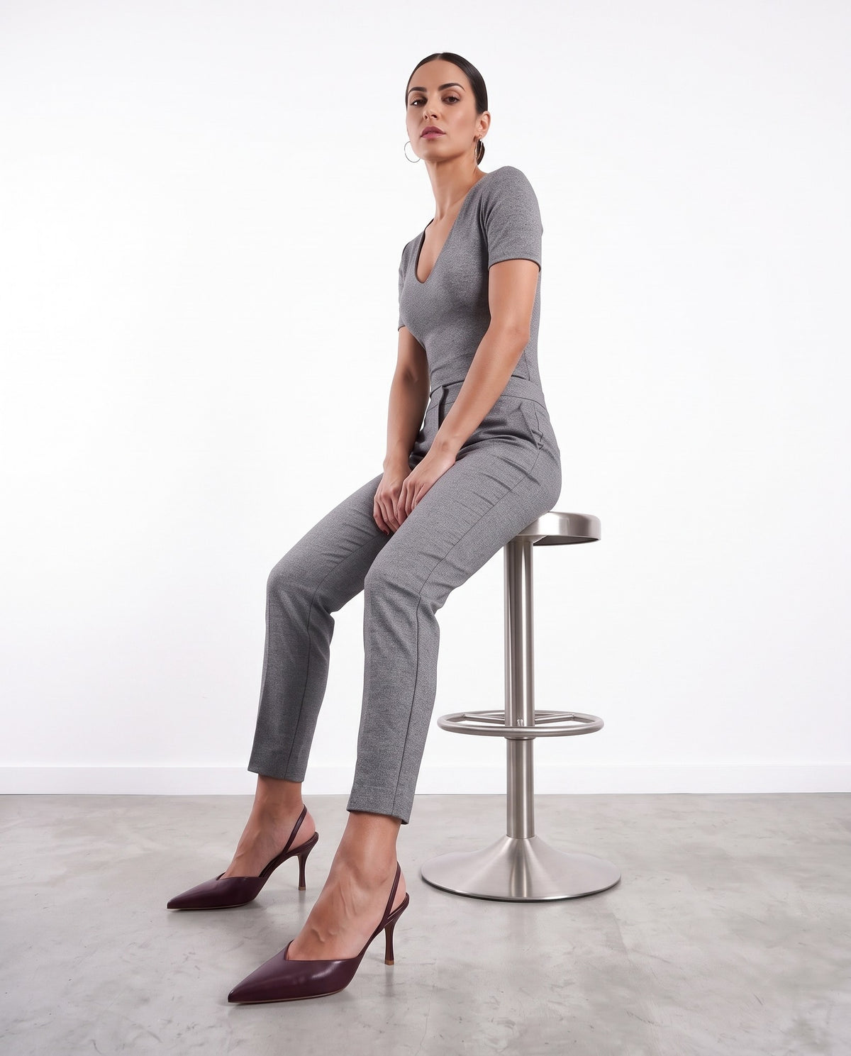 Modella seduta su sgabello in acciaio, indossa décolleté slingback color vino con tacco a spillo.
