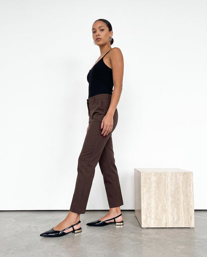 Modella in abito nero e pantaloni cioccolato cammina con slingback nere in vernice, tacco dorato.