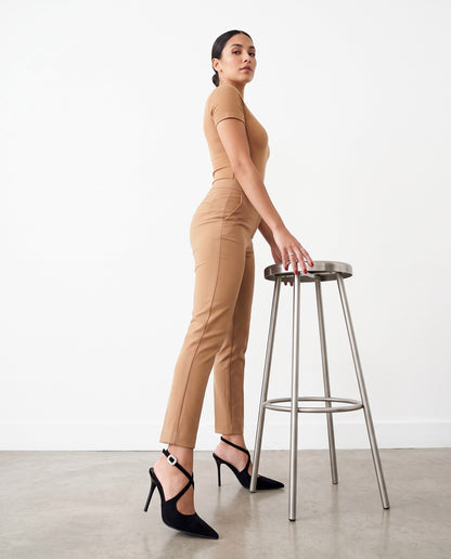 Modella di profilo con decolleté nero slingback, appoggiata a uno sgabello in acciaio.