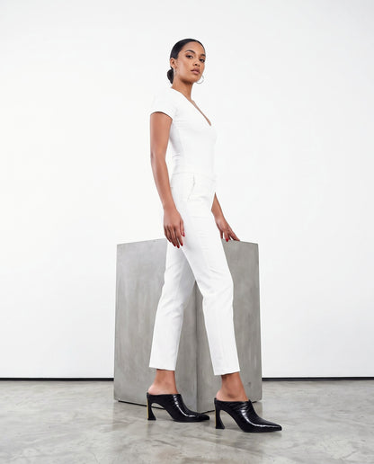 Modella in abito bianco con mule neri lucidi a punta, accanto a blocco di cemento, studio chiaro