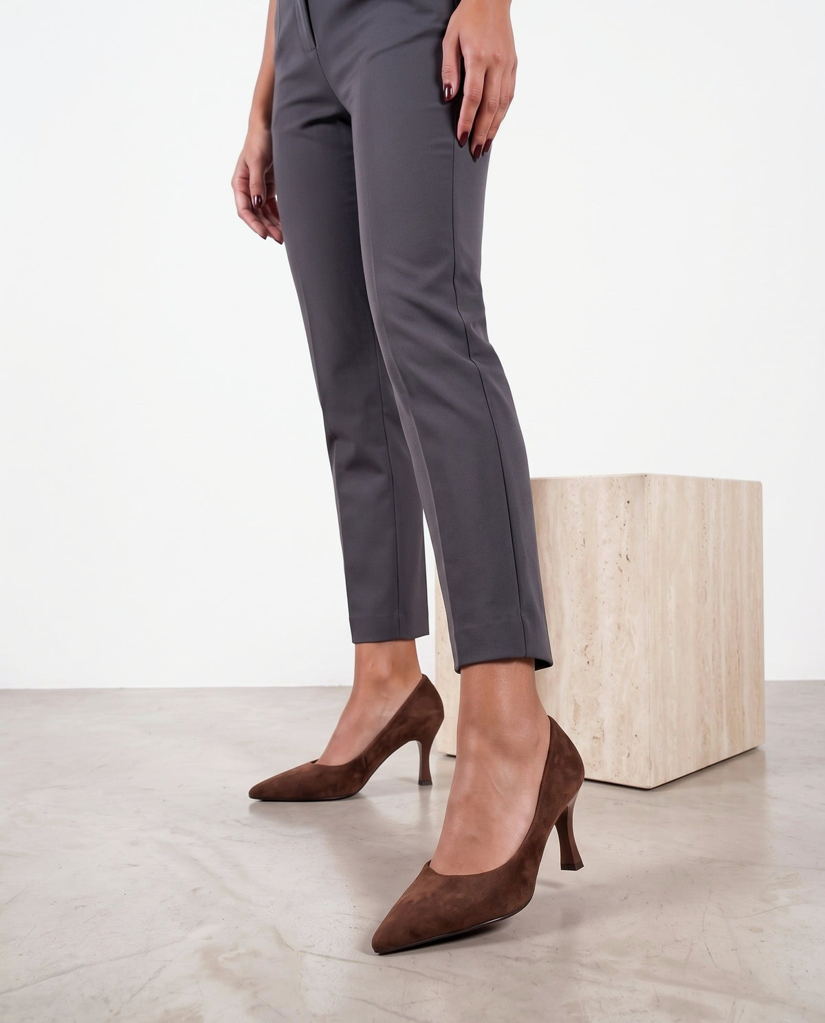 Gambe di modella con décolleté scamosciate color camel/marrone, cubo in travertino sullo sfondo