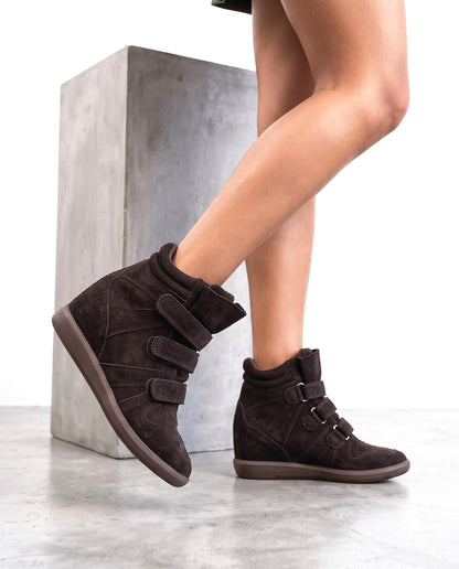 Dettaglio ravvicinato di due sneaker con zeppa in camoscio marrone scuro, su blocco di cemento, vista tre quarti.