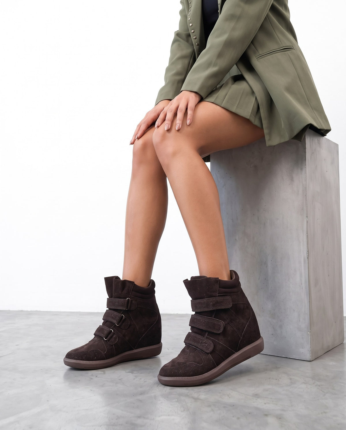 Modella seduta su blocco di cemento con sneakers wedge marroni in camoscio con cinturini a strappo